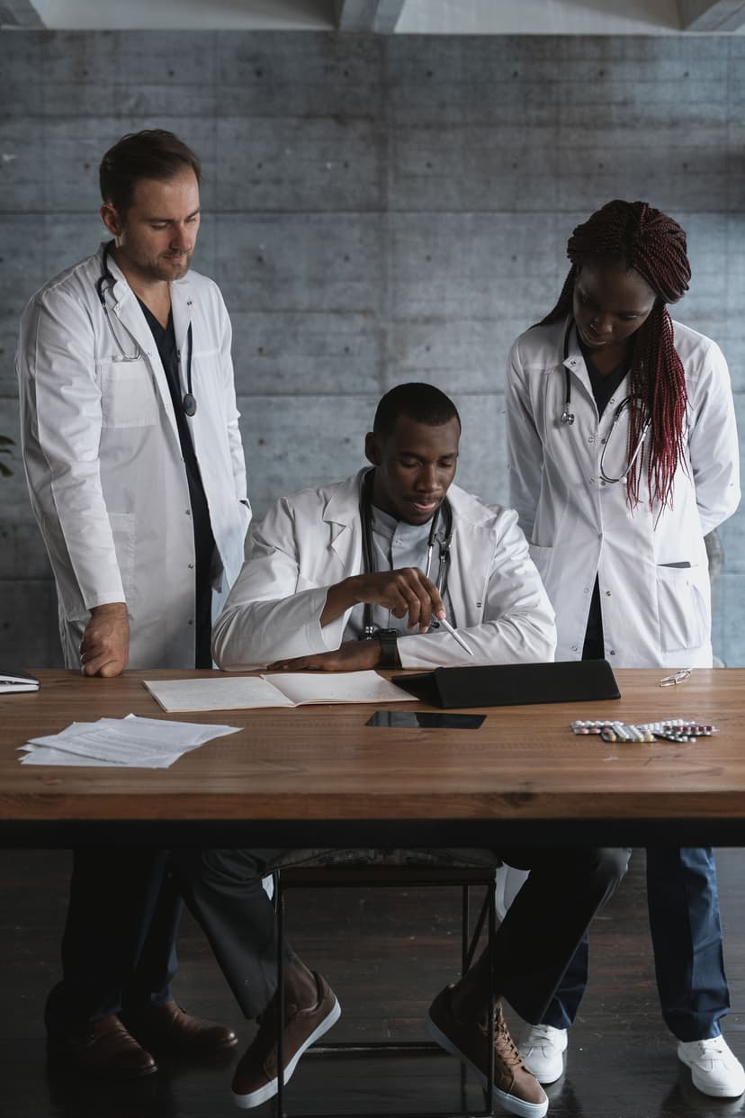 Three physicians in white coats review papers together at a table.